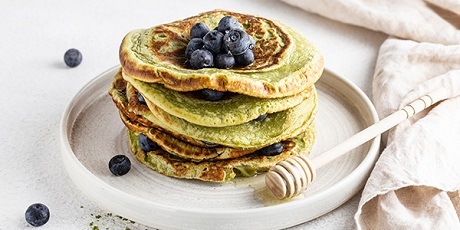 Pila di pancake verdi con mirtilli, miele e cucchiaio.